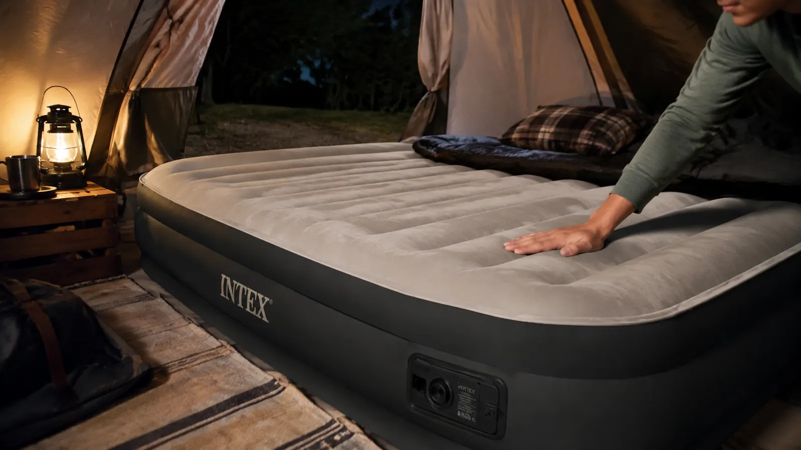An inflated Intex queen air mattress set up inside a tent at night, a hand pressing the surface to check how firm it holds